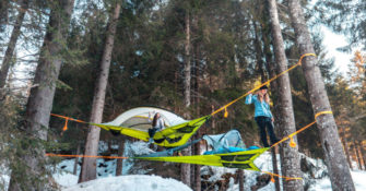 two tents suspended in air over forest floor covered in snow